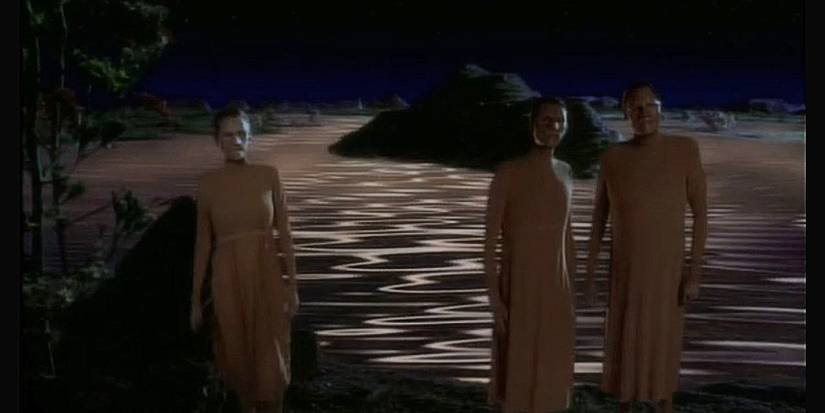 Three androgynous aliens in flowing robes, standing before a shimmering flesh-colored ocean.