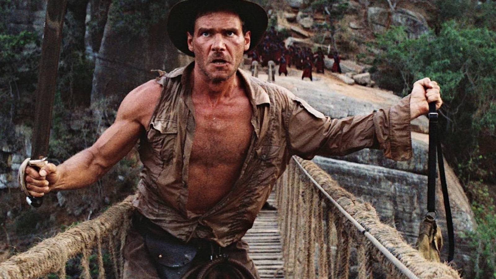 indiana jones ready to throw the ancient stones off a bridge while he holds a sword