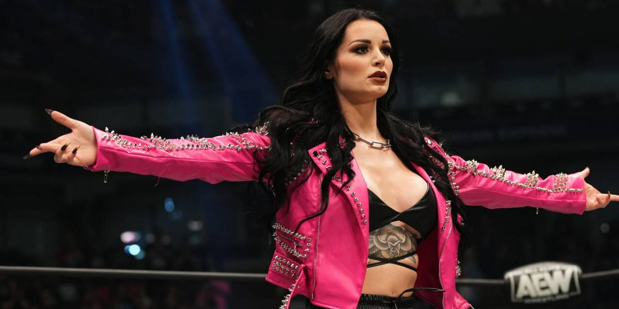 Former WWE and current AEW star Saraya in a pink jacket with her arms spread as she addresses the crowd from the ring.