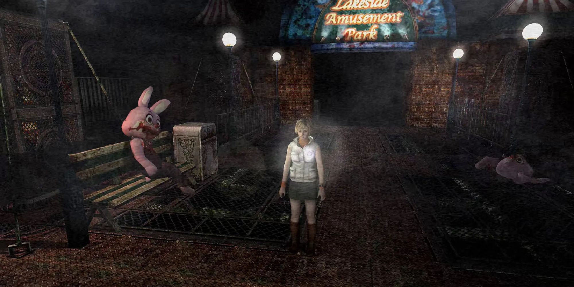 Heather standing in the nightmare version of Lakeside Amusement, a giant Robbie the Rabbit slumped on the adjacent bench, blood around its mouth. 