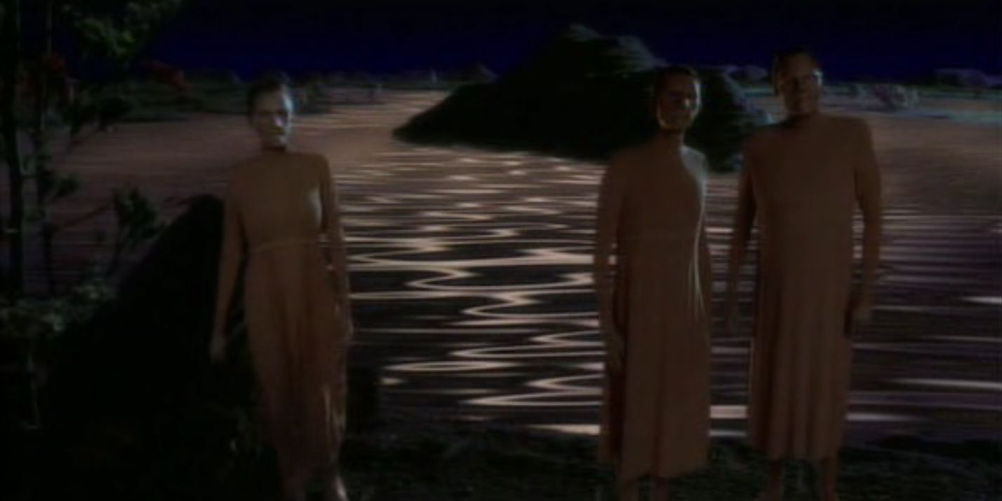 Three androgynous aliens in flowing robes, standing before a shimmering flesh-colored ocean.