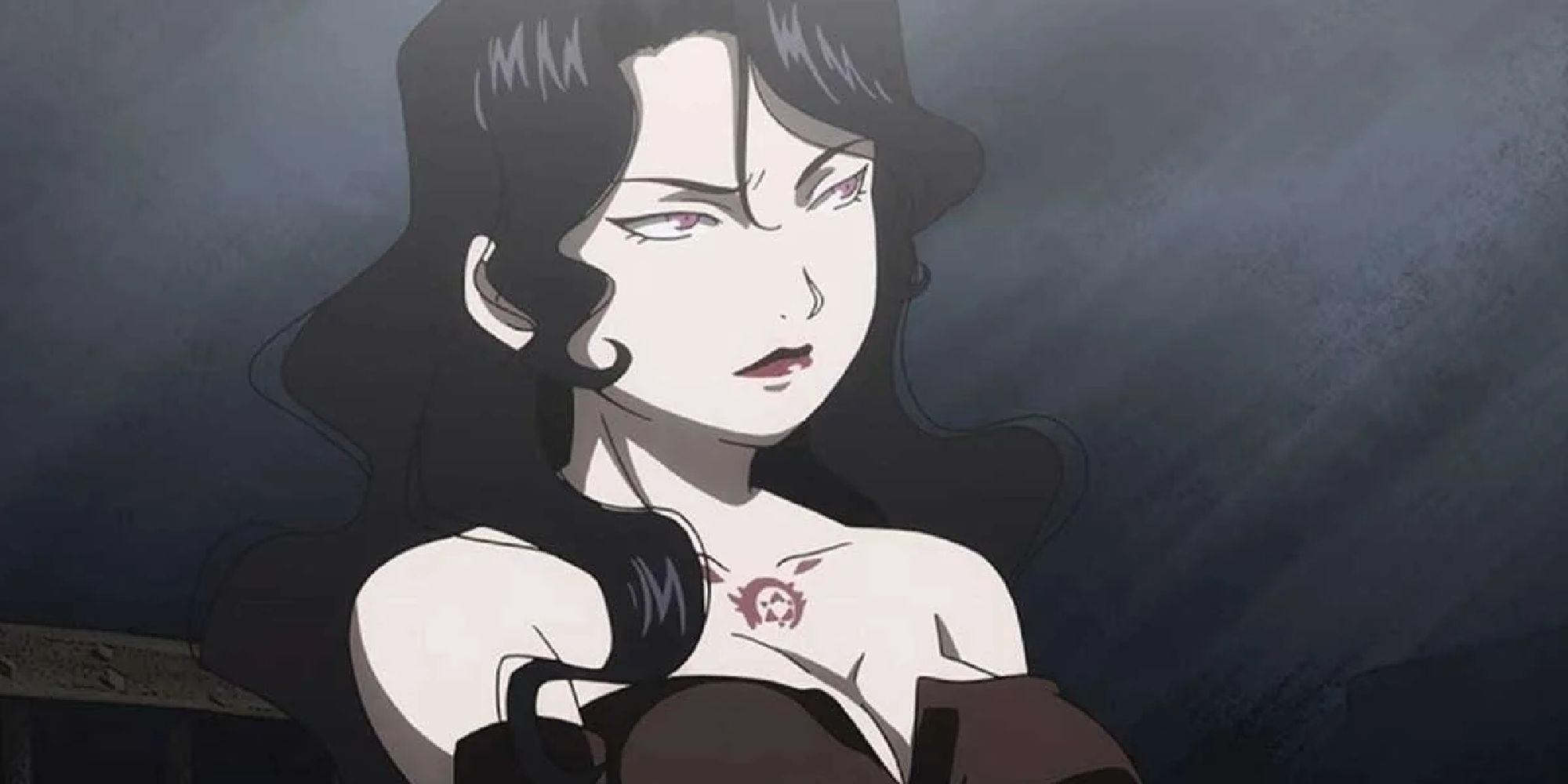 Lust wears a partial scowl on her face as she looks off to the side, standing in a dark room. 