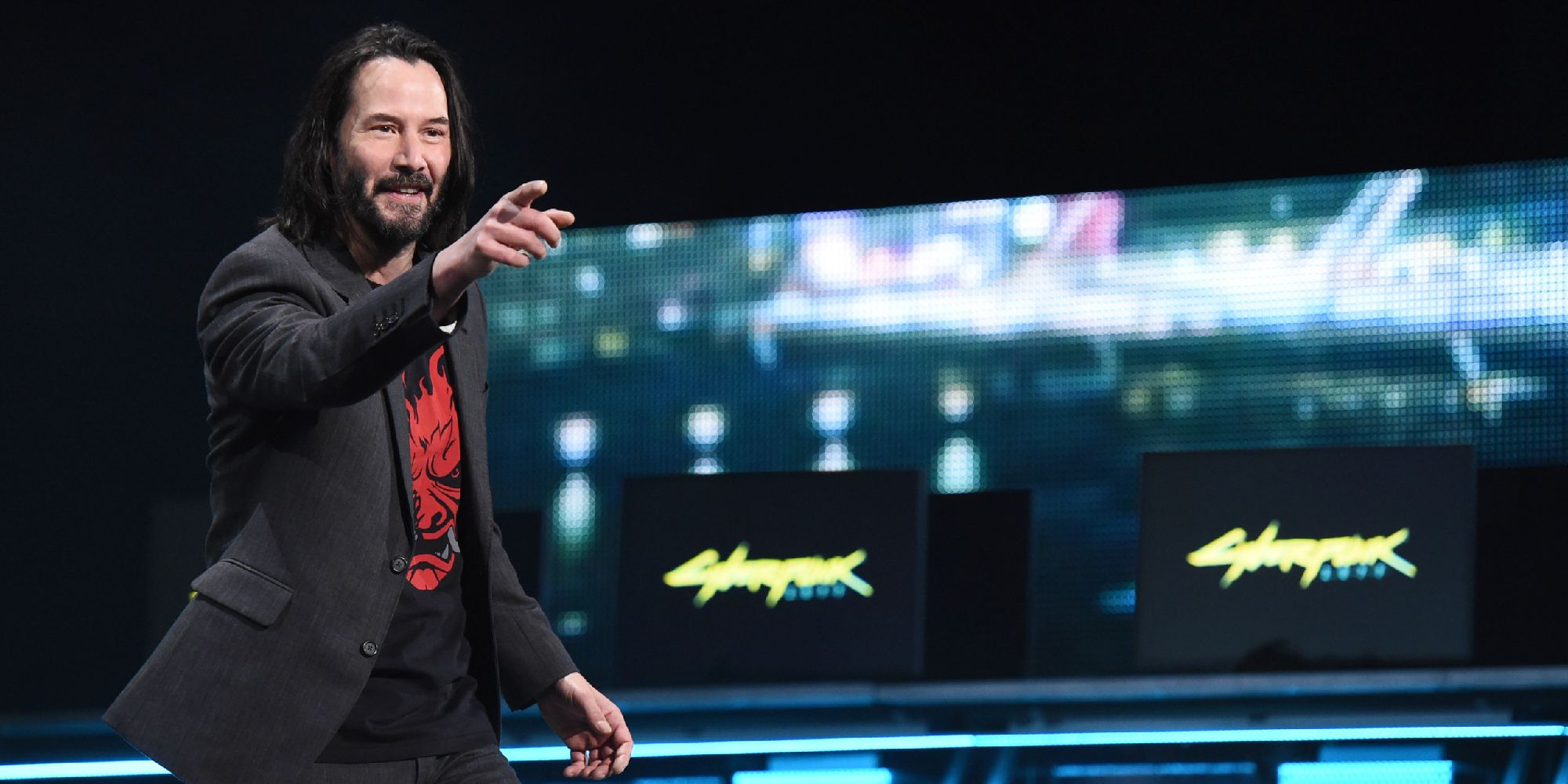Keanu Reeves at the E3 announcement for Cyberpunk, smiling and pointing forward. 