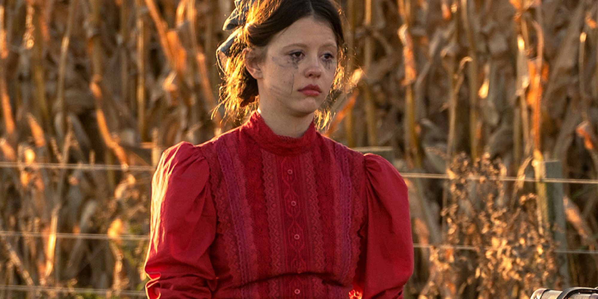 Mia Gith staring as Pearl, standing in the red dress with mascara tears staining her face.