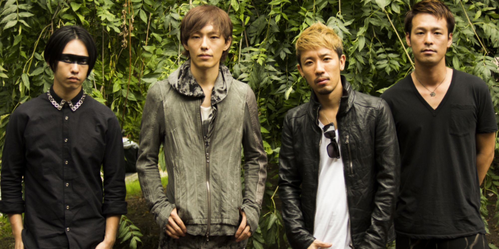 four men stand with a back drop of leaves