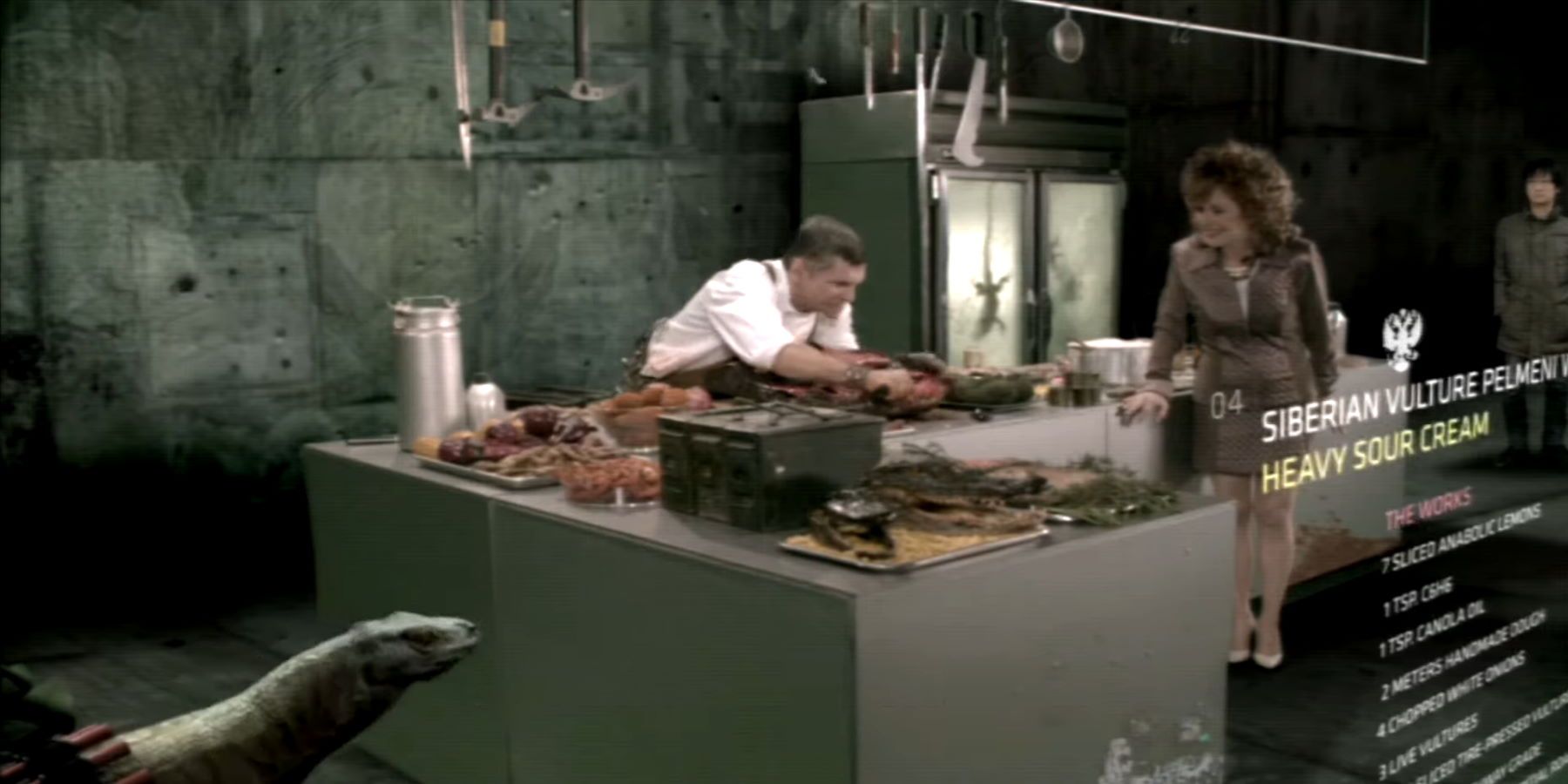 Two cooking hosts preparing a meal in a dirty kitchen and a lizard to the left. Behind the on-screen ingredients is Hideo Kojima in the corner wearing a coat