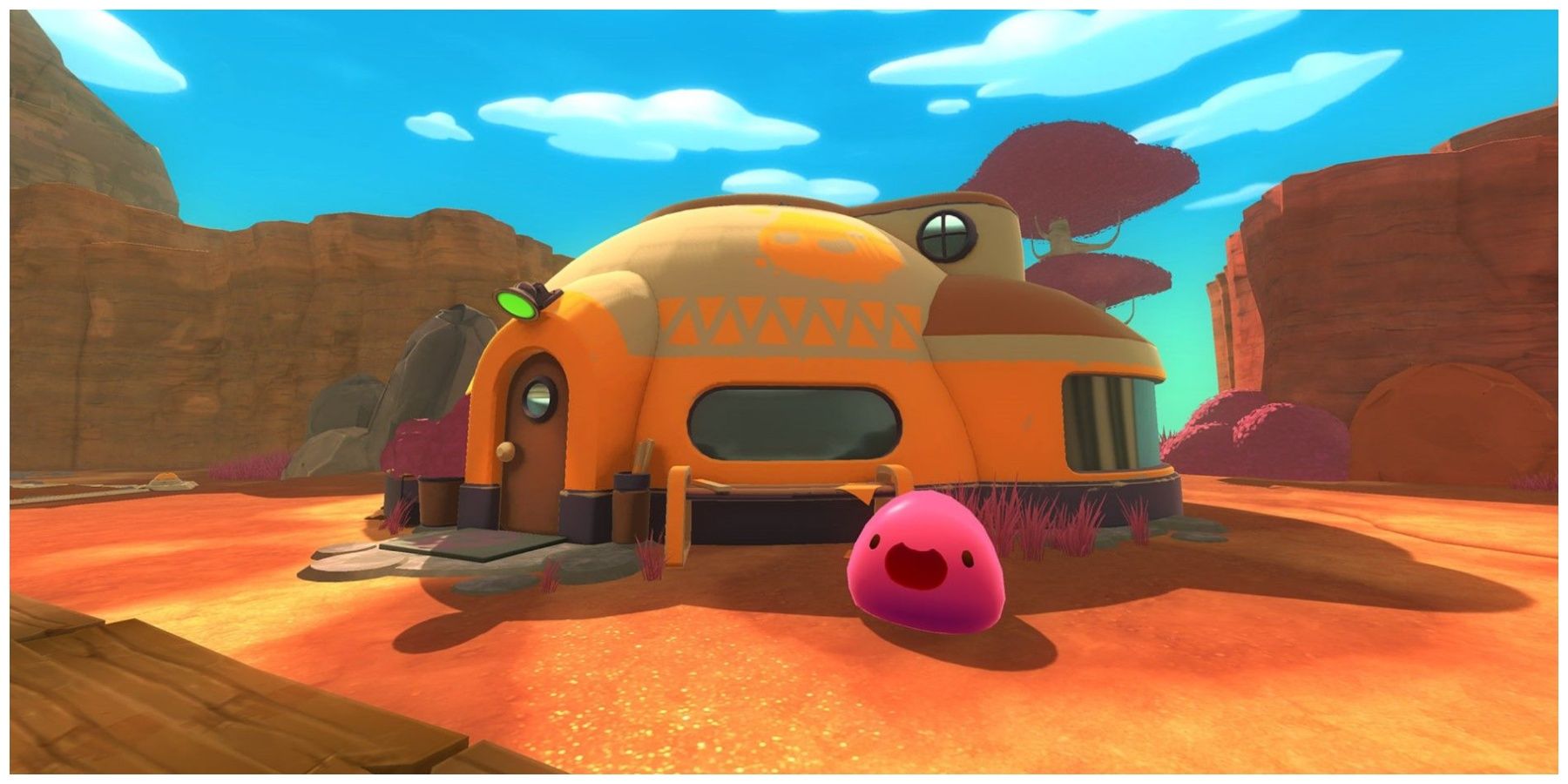 A happy pink slime in front of a yellow hut in a desert in Slime Rancher