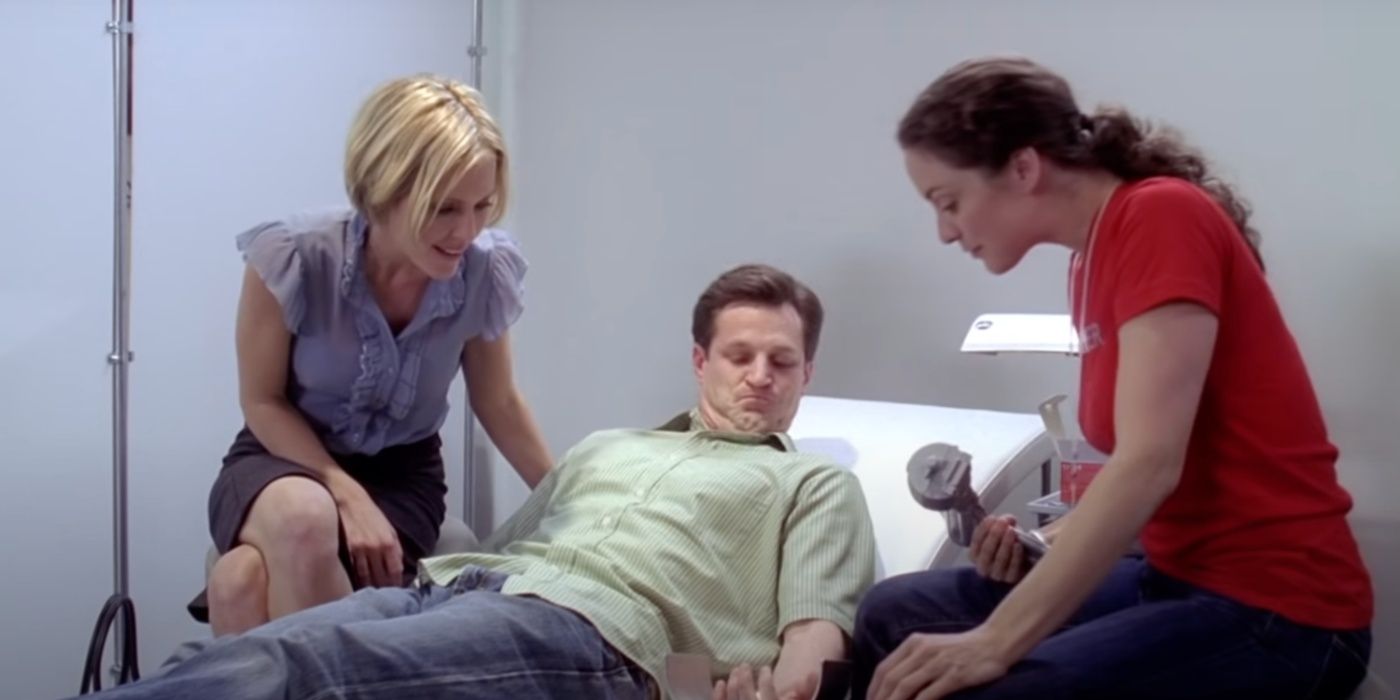 Two women watch as a man inspects his arm which a device was just inserted into