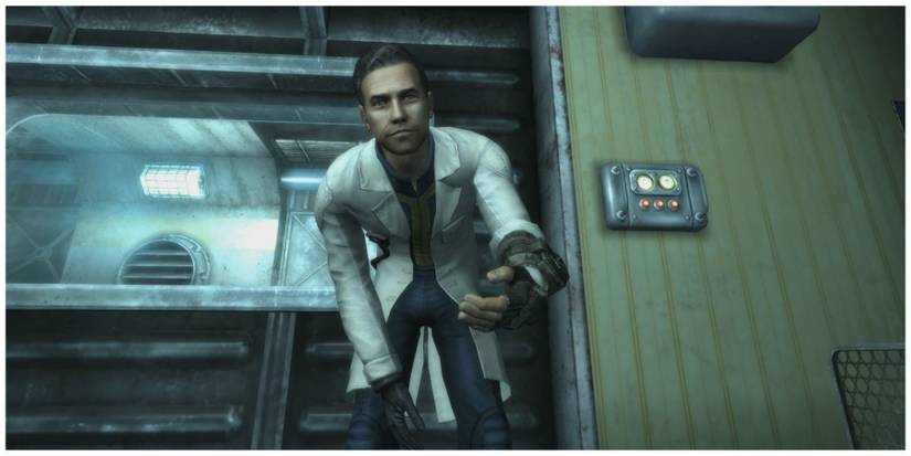 A man in a white lab coat crouching down to the camera and holding out a hand