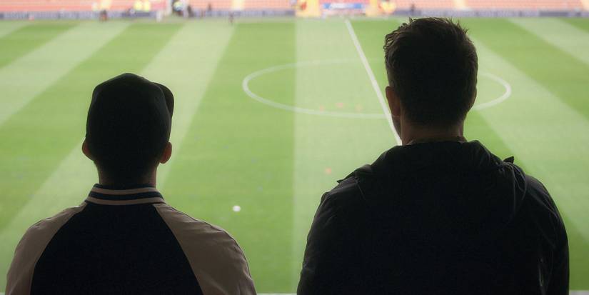 Photo of Rob McElhenney and Ryan Reynolds on Racecourse Ground stands from behind.