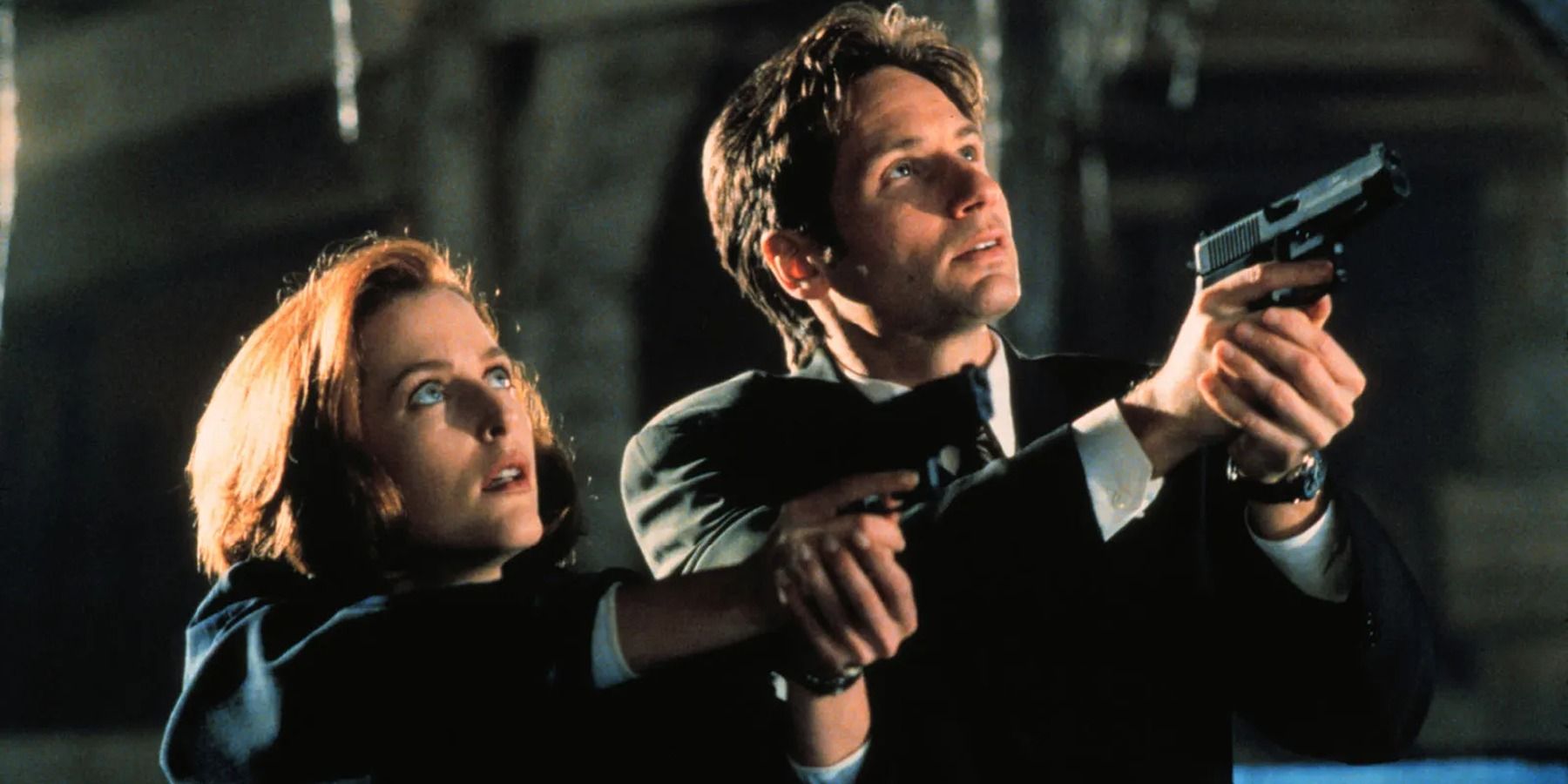 Dana Scully (Gillian Anderson) and Fox Mulder (David Duchovny) aiming their guns upwards.