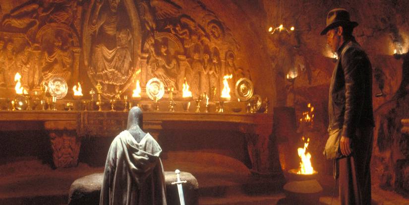 Indiana Jones stares at a kneeling crusader in a room filled with ancient grails