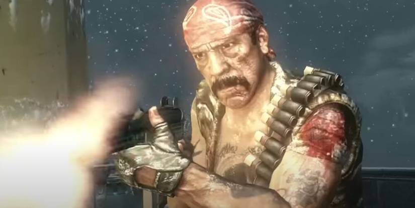 Danny Trejo with a red bandana and ammo bandolier firing an SMG