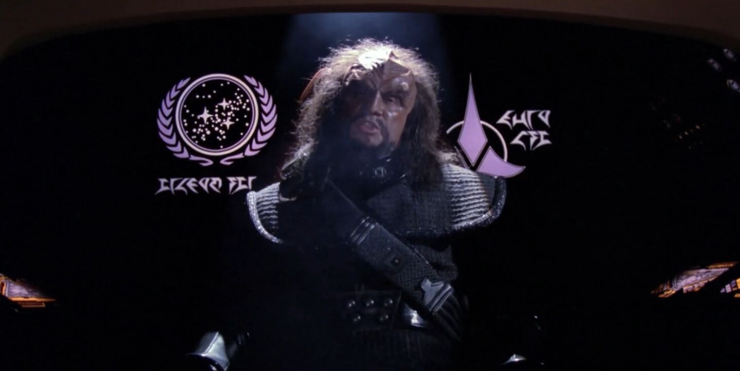 A Klingon sits in front of the Federation flag in Star Trek's "Heart of Glory".
