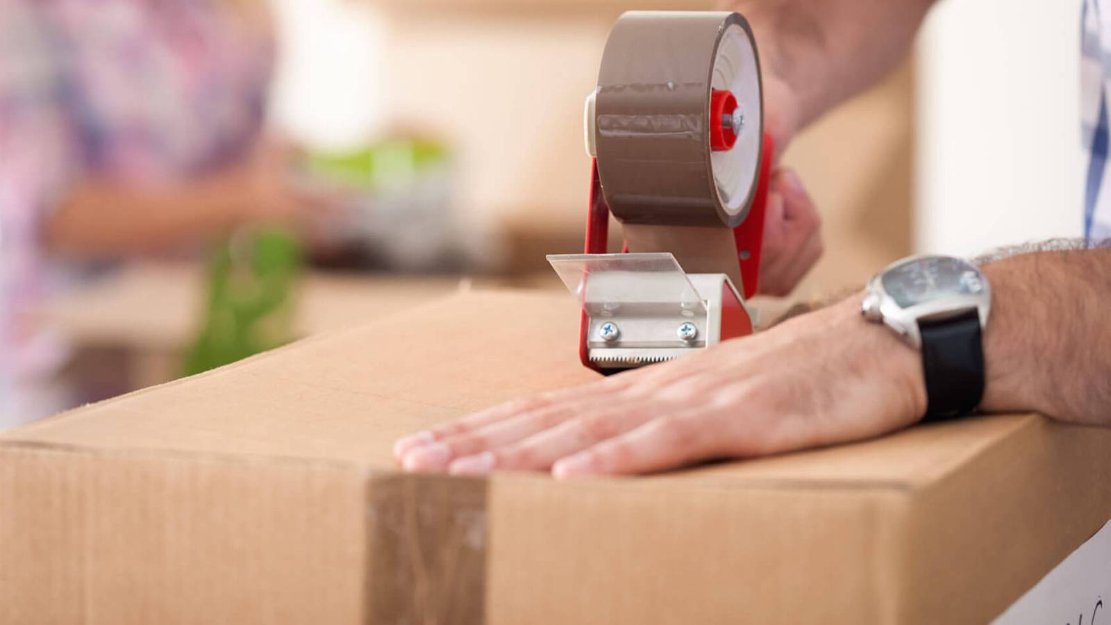 A stock image of someone taping a cardboard box closed while wearing a blue and white flannel shirt.