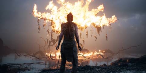 Senua stands in front of a  burning tree with hanging bodies in Hellblade Senua's Sacrifice