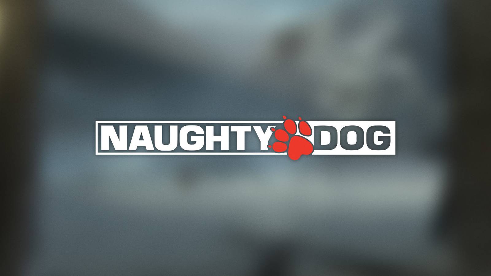A white and red Naughty Dog logo placed in front of a blurry grey background.