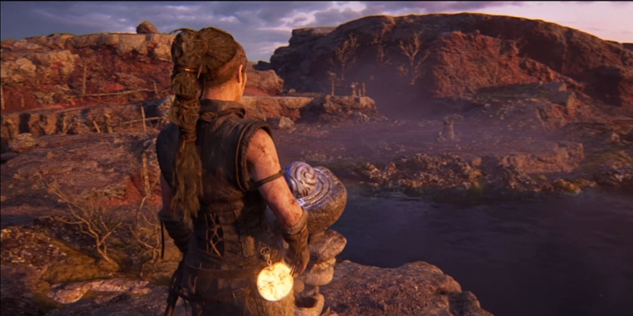 Senua standing by a stone pedestal next to a lake in Hellblade 2