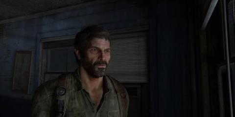 Joel stands in a dimly lit room, deep in thought and determination, from a quiet but intense moment in The Last of Us.