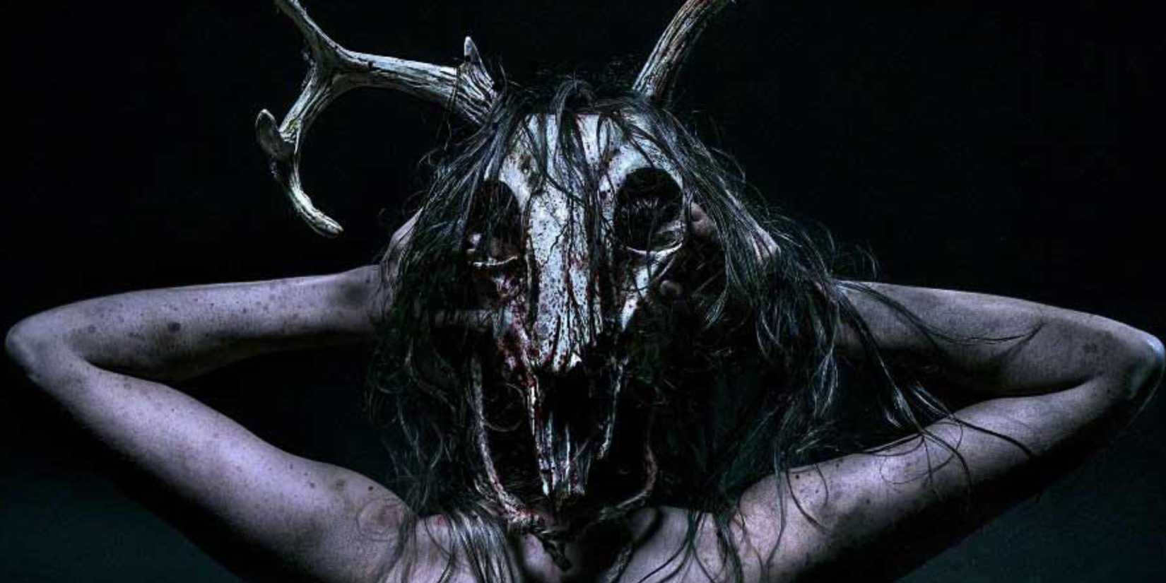 Someone wears a dirty, bloodied deer skull with hair hanging down