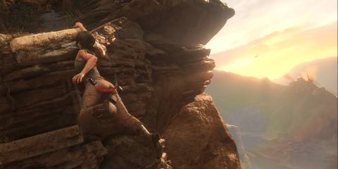 Lara Croft hanging from a ledge with a sunset in the background 