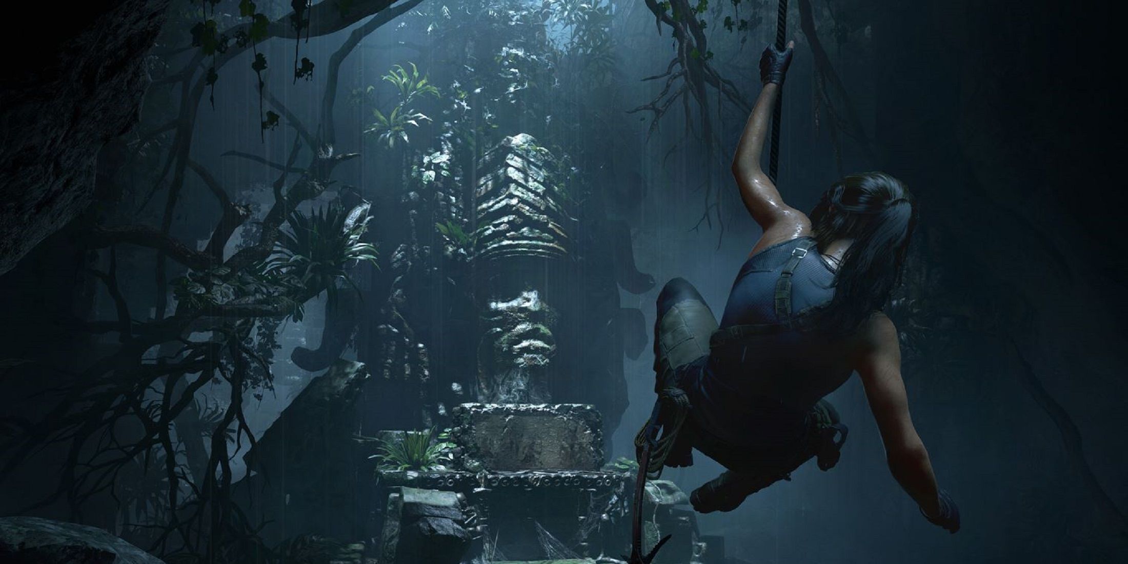 Lara Croft swings on a rope in a dark, overgrown cave in Shadow of the Tomb Raider