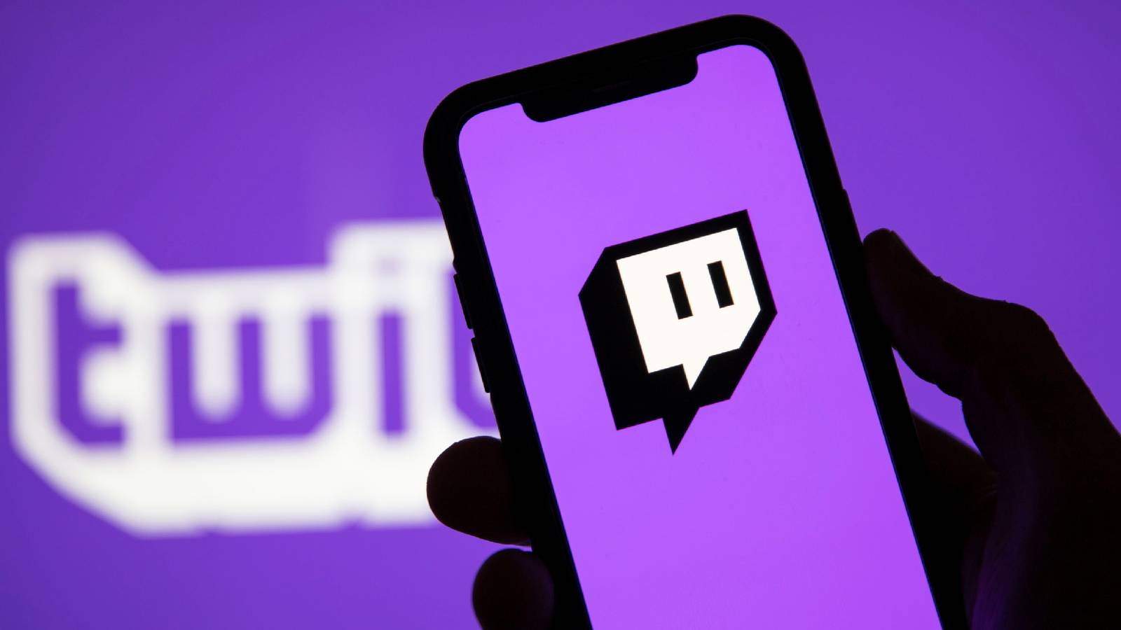 An image of a hand holding a phone displaying the Twitch logo with an alternate Twitch logo in the background.