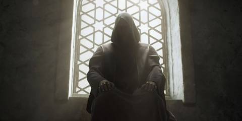 Hooded character sitting in front of a patterned window in Diablo 2: Resurrected