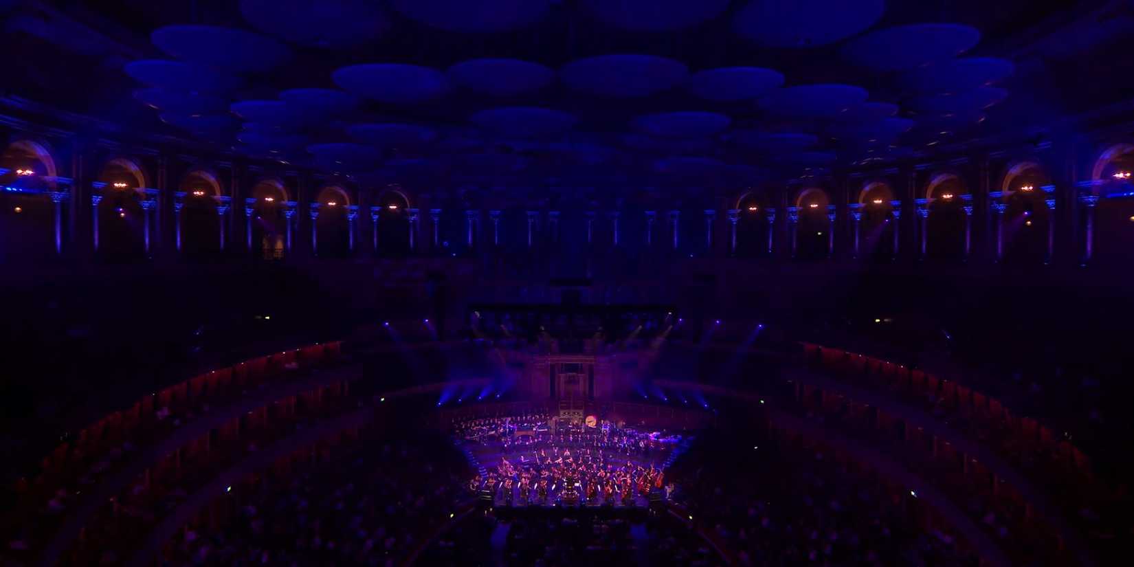A Frame Showing The Orchestra From The PlayStation In Concert Performance Highlighted By Studio Lights