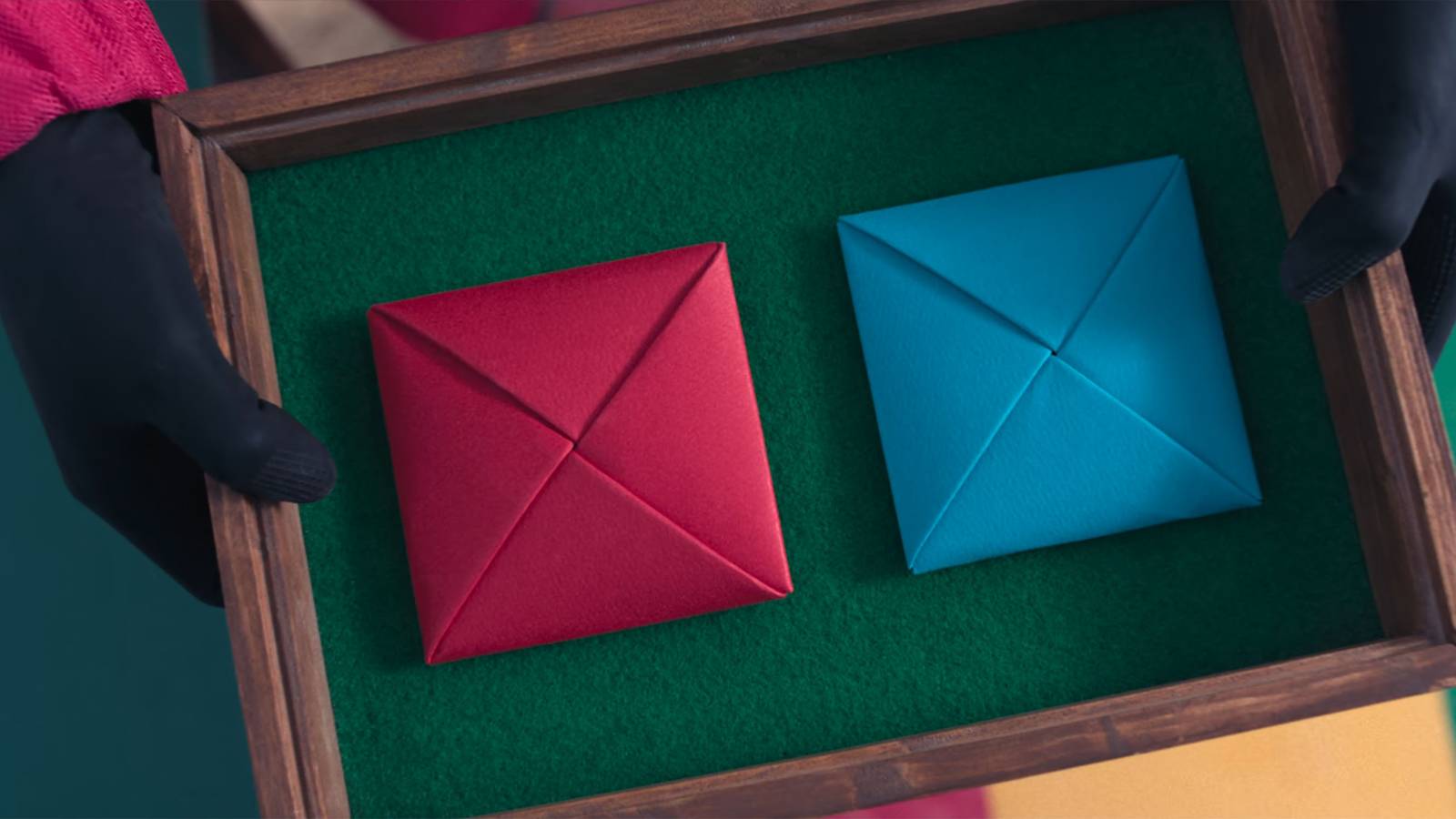 A red and blue Ddakji tile gets presented in a green felt box in Squid Game.
