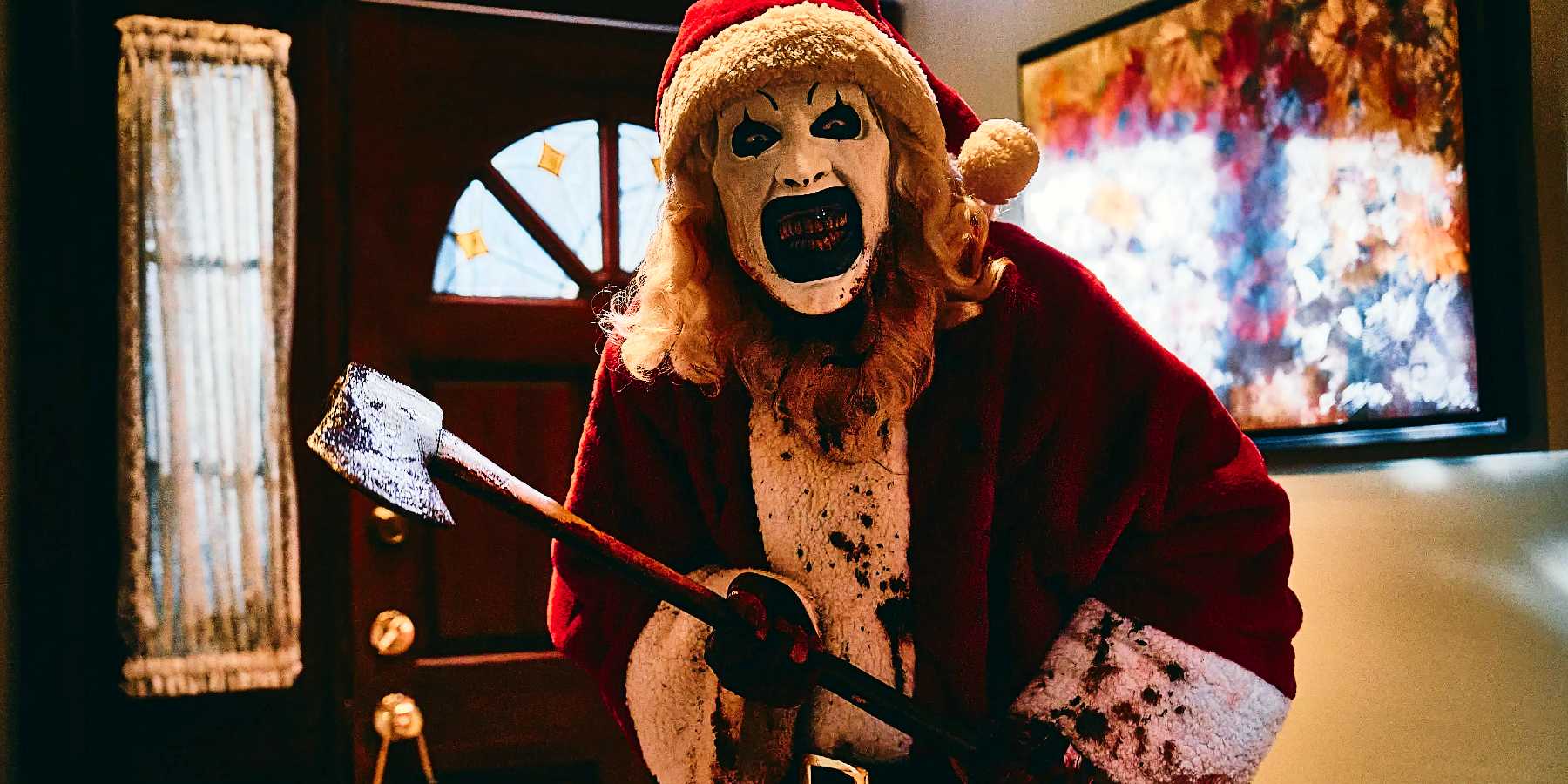 David Howard Thorton as Art the Clown in a bloody Santa Clause costume, holding an axe in his victim's home from Terrifier 3