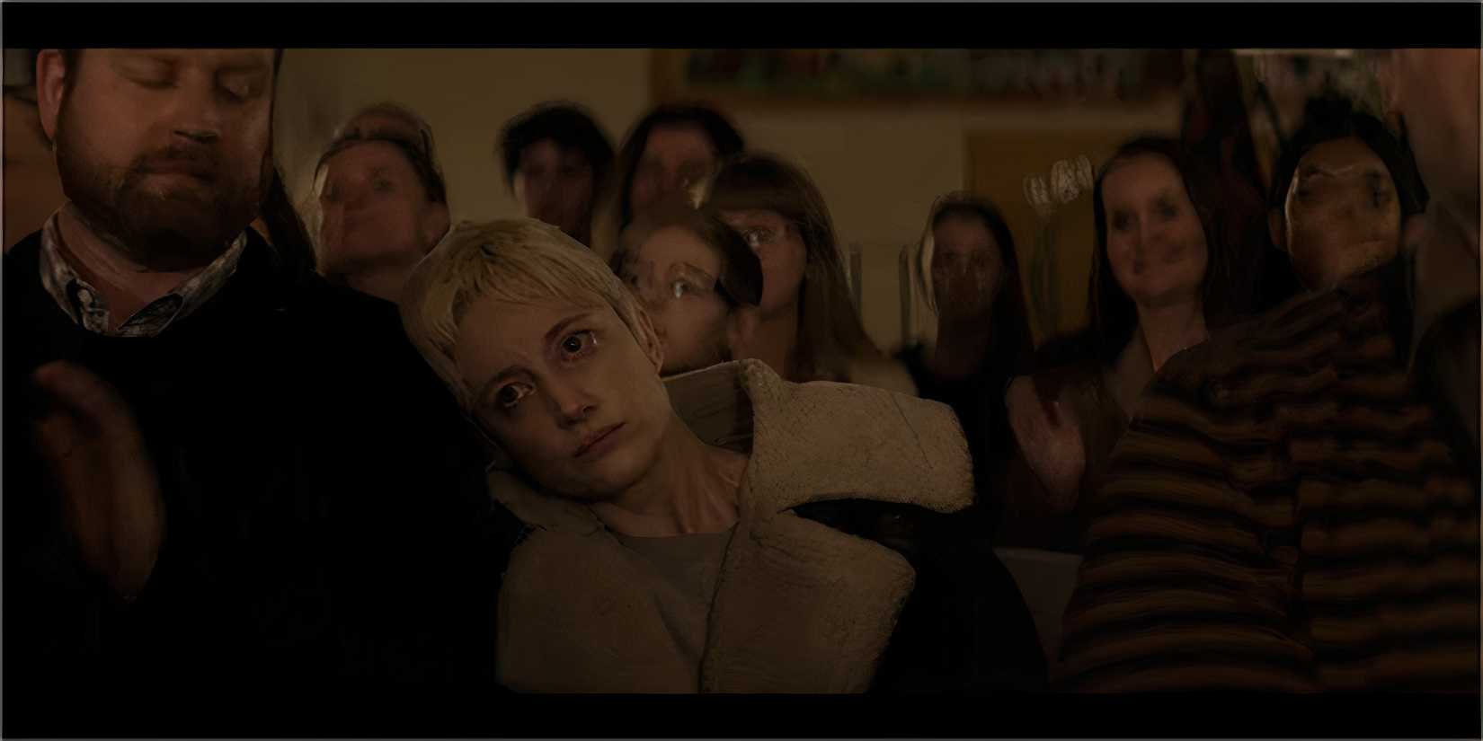 A blonde woman looking detached while sitting among a clapping audience.