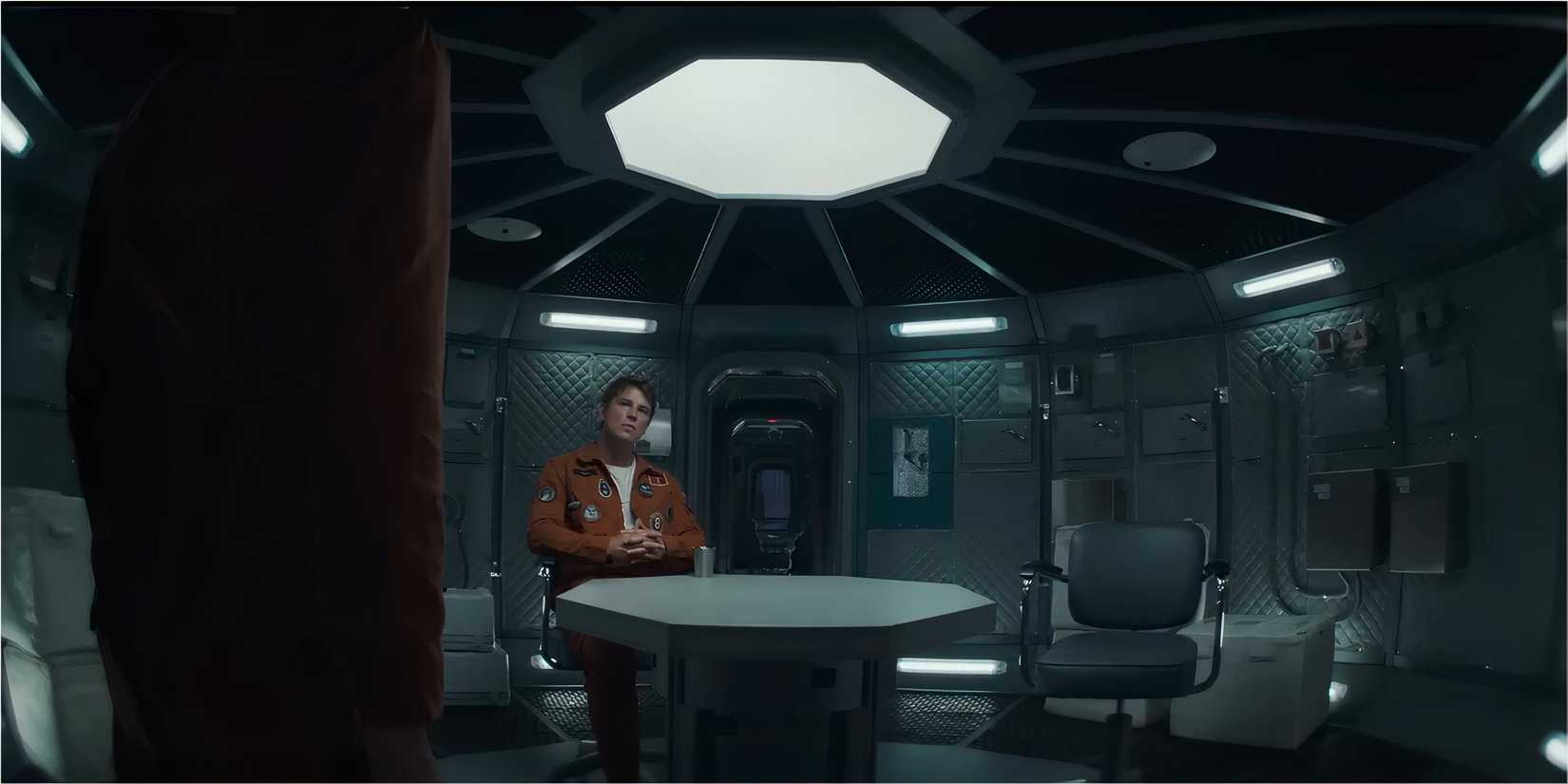 An astronaut in an orange jumpsuit sitting in a futuristic space station.