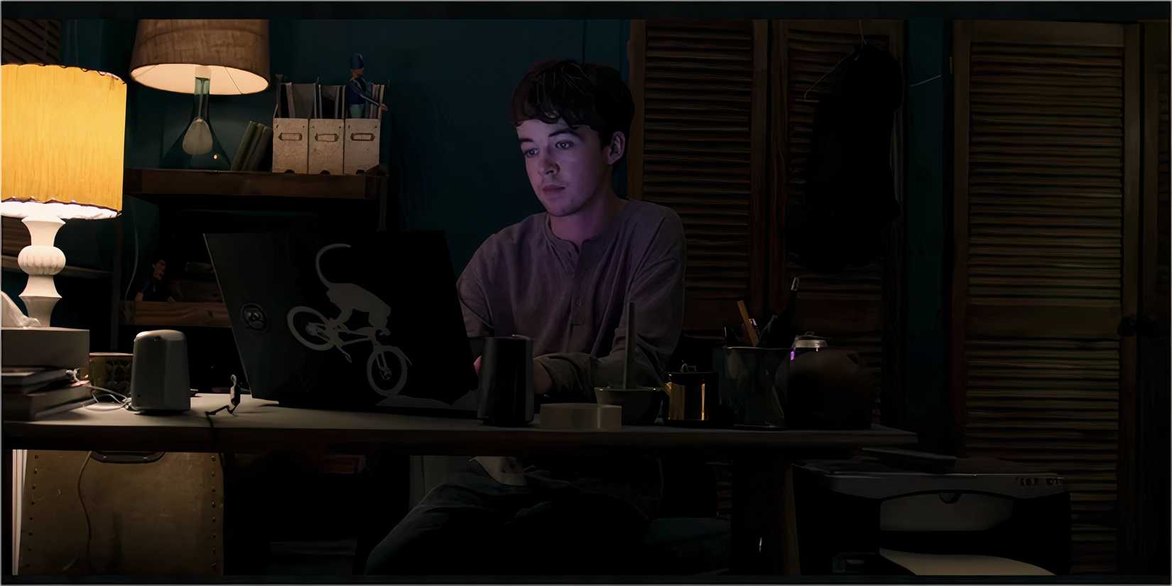 A young man sitting at a desk, staring at his laptop screen.