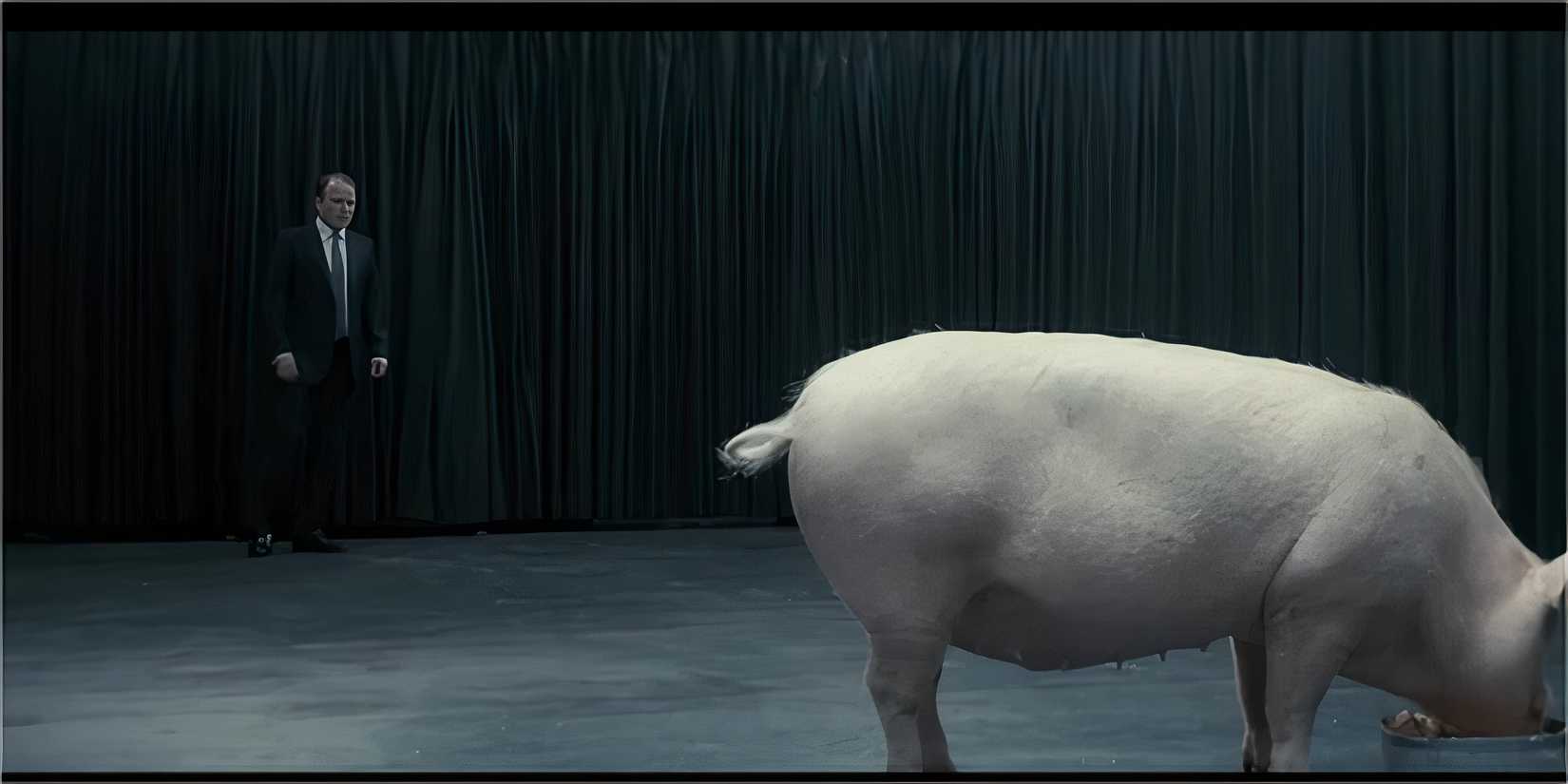 A man in a suit standing near a pig in a dark room.