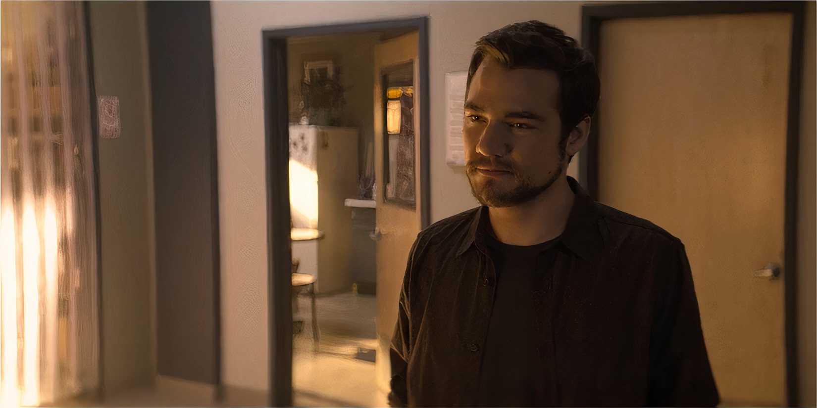 A man with a beard stands in a softly lit hallway