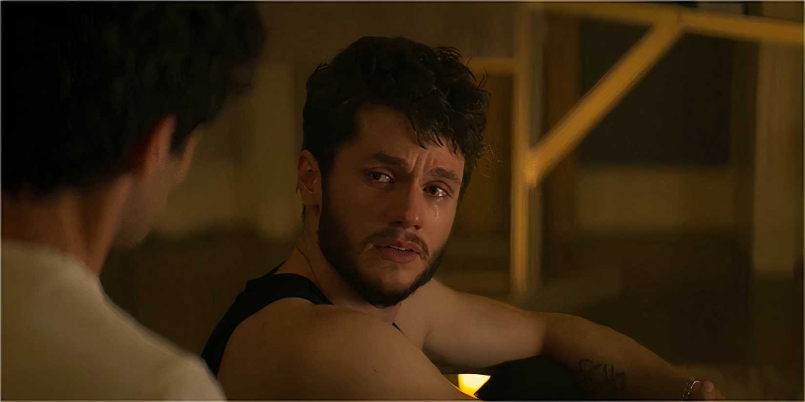 A man with curly hair sits on the floor, teary-eyed.