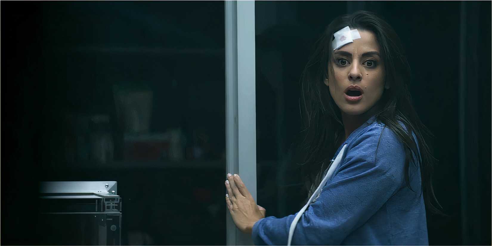 A woman in a blue hoodie looks alarmed as she opens a glass door in a dark room