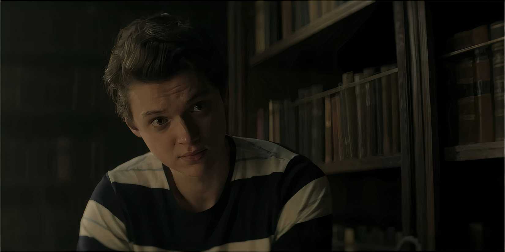 A young man sits in a library with a serious expression