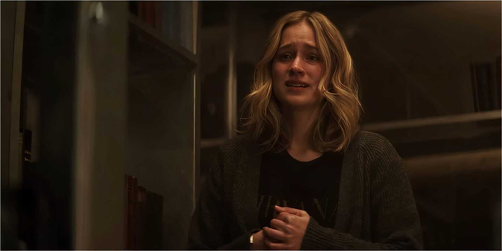 A blonde woman stands crying in a dimly lit room