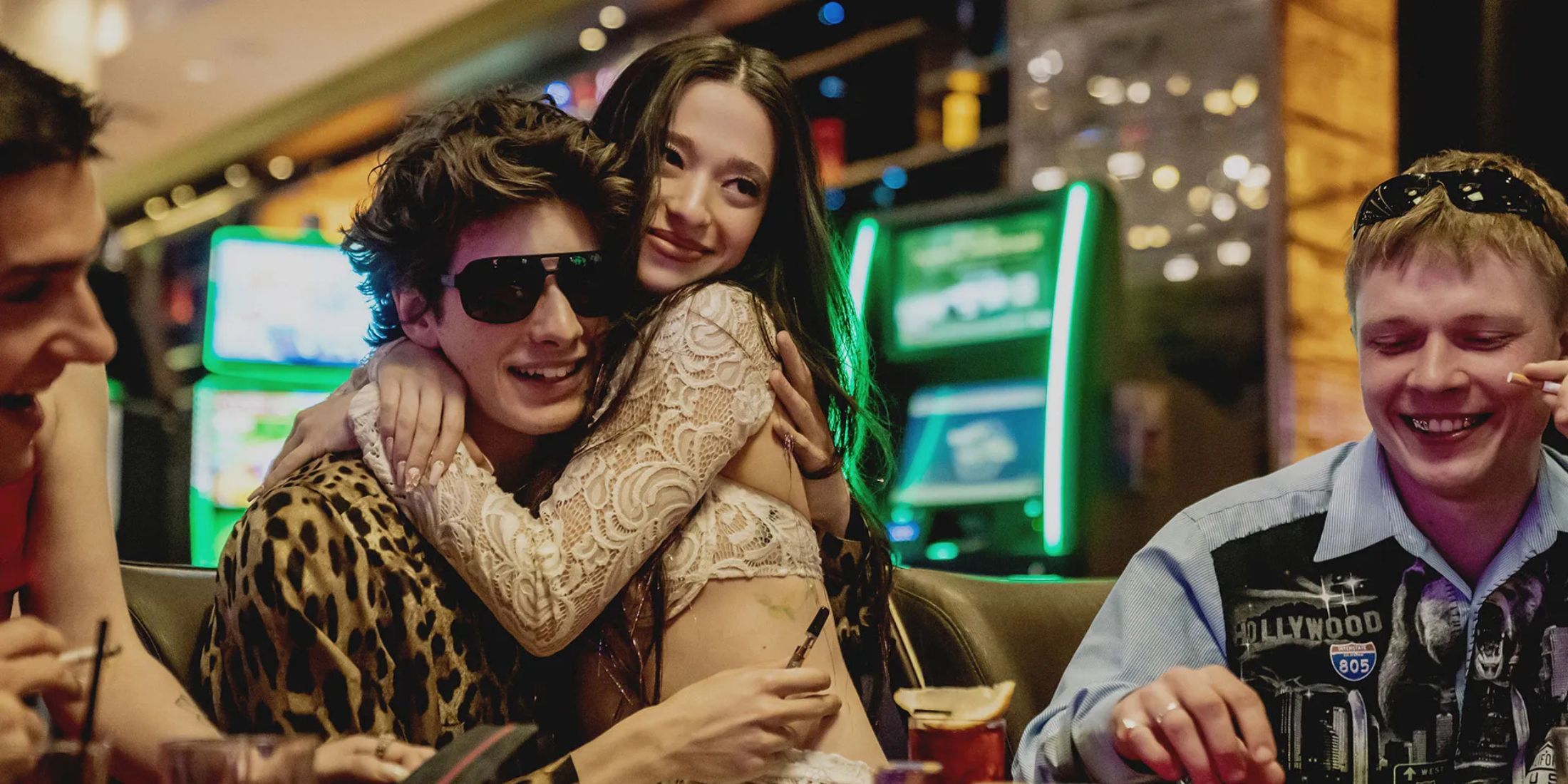 Two characters from Anora hugging while sitting at a casino table