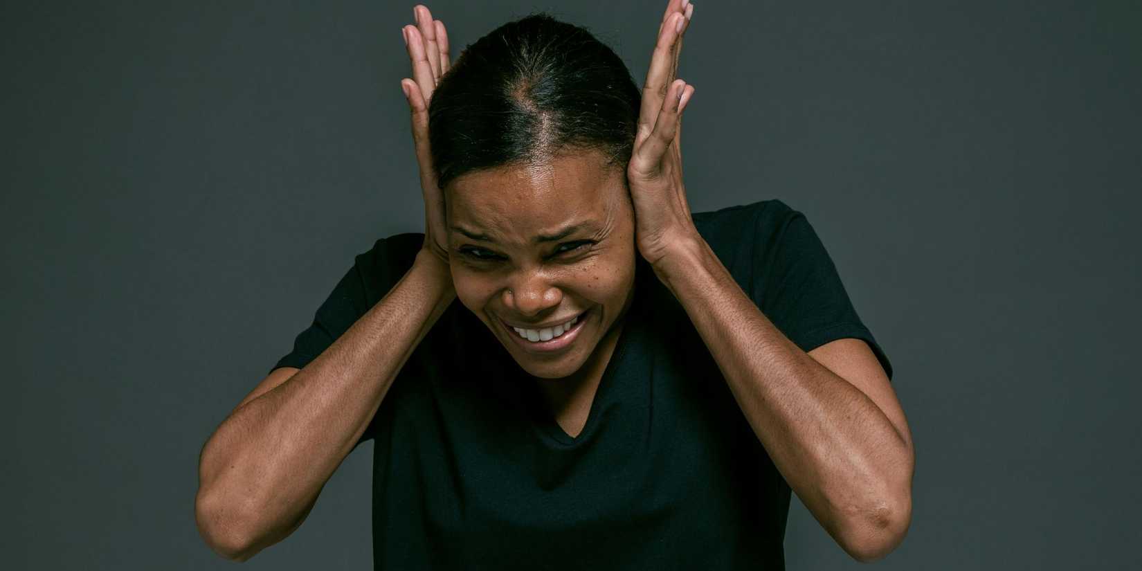 Woman dramatically covering up her ears due to noise.