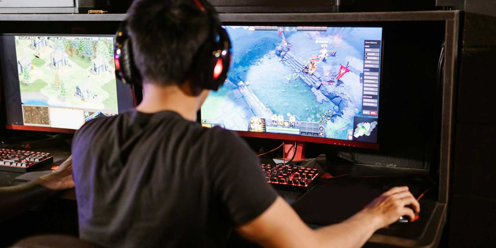 Image of a man playing video games on a PC on a desk. he is wearing headphones. 