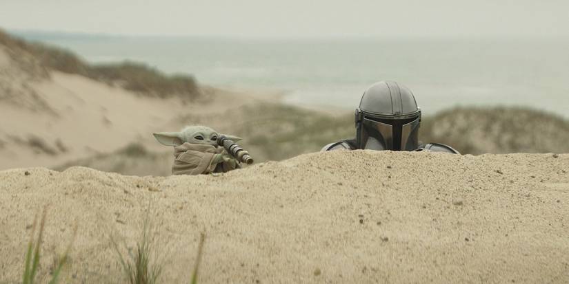 Grogu and Din Djarin peer over a sand dune in The Mandalorian & Grogu