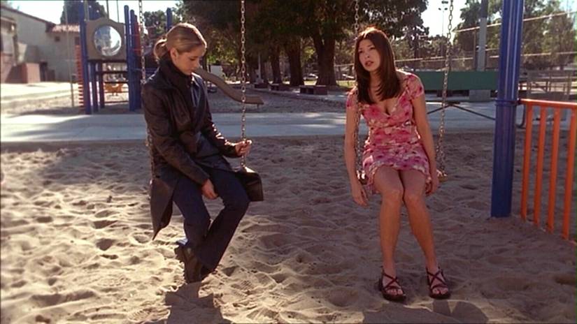 Buffy and April the robot sit on some swings in the park
