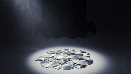 Broken video game disc with Xbox in the background