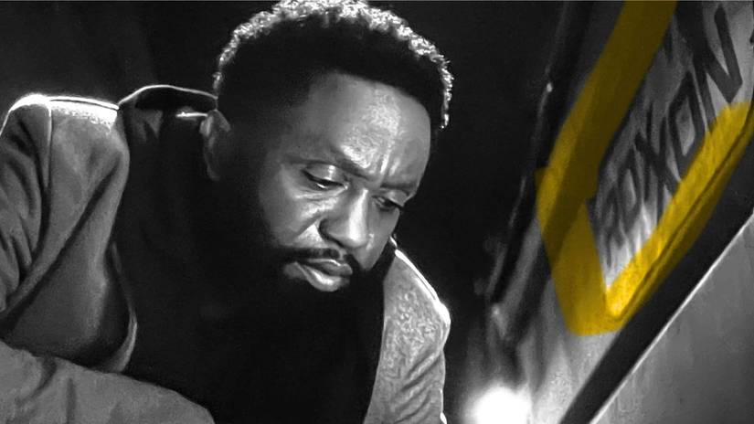 Doorman inspects the ground underneath a yellow-outlined Roxxon sign in an otherwise black-and-white shot from Wonder Man