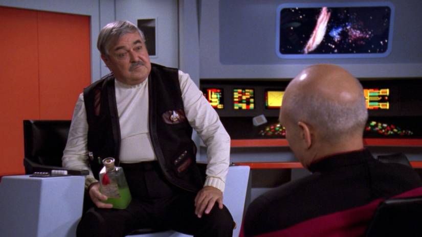 Scotty sits in the captain's chair talking with Picard in a holodeck recreation of the original Enterprise bridge in Star Trek: The Next Generation 