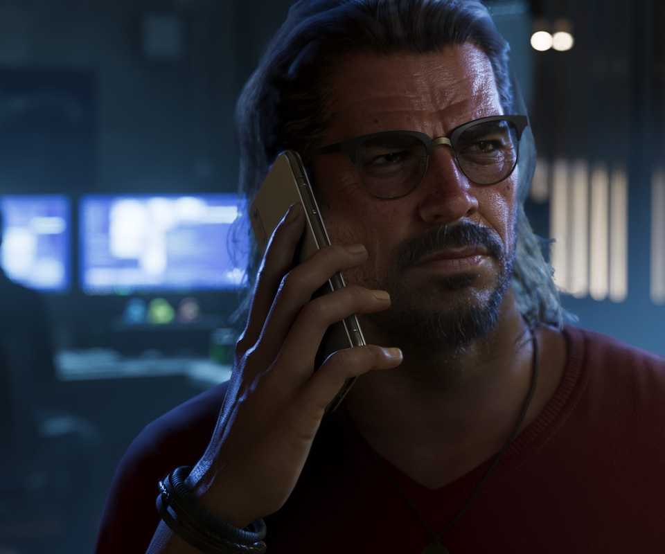 A screenshot of Raul Bautista from Grand Theft Auto 6 talking on his mobile phone with an accomplice in the background on a computer.