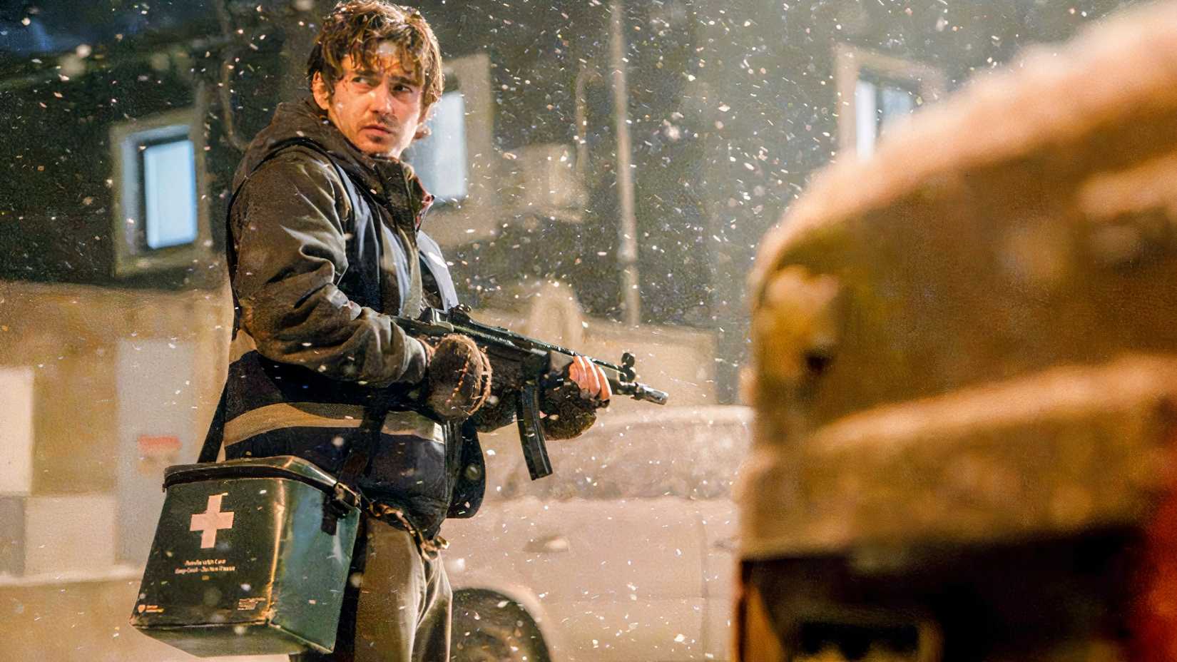 Austin Abrams as Bryan in Resident Evil 2026 standing in the snow, among abandoned cars, while holding an MP5 with his green and white medical bag at his side